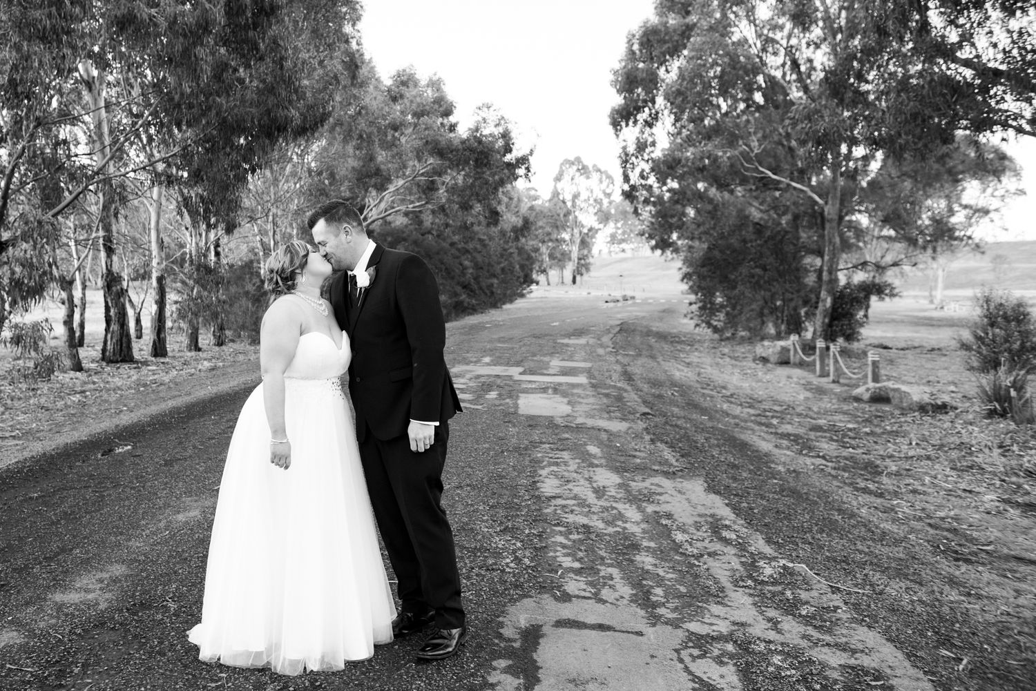 A couple in formal wedding attire walks along a tree-lined path in black and white photography.
