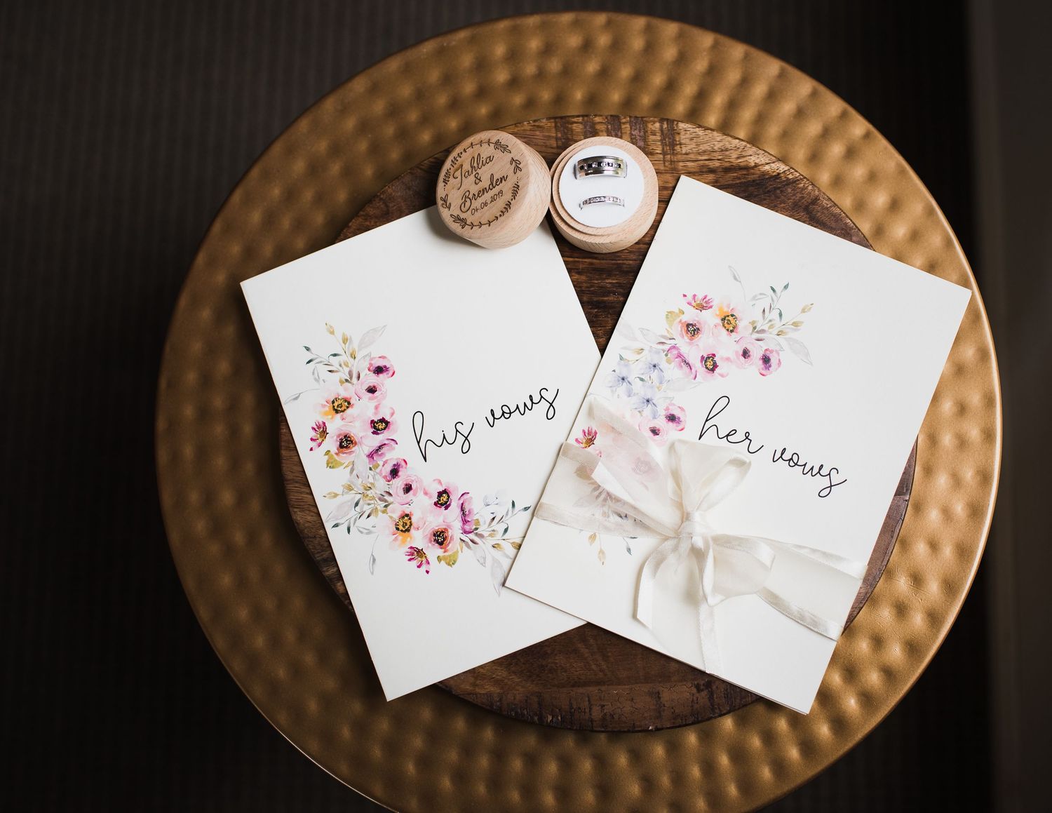 Wedding invitations with watercolor floral designs and calligraphy displayed on a textured copper surface.