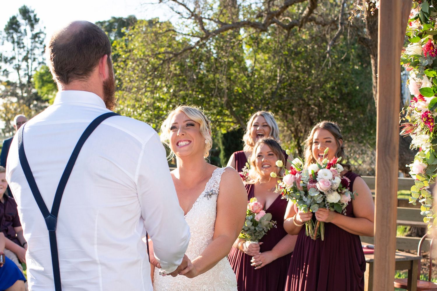 Outdoor wedding celebration with guests in suspenders under wooden pergola.