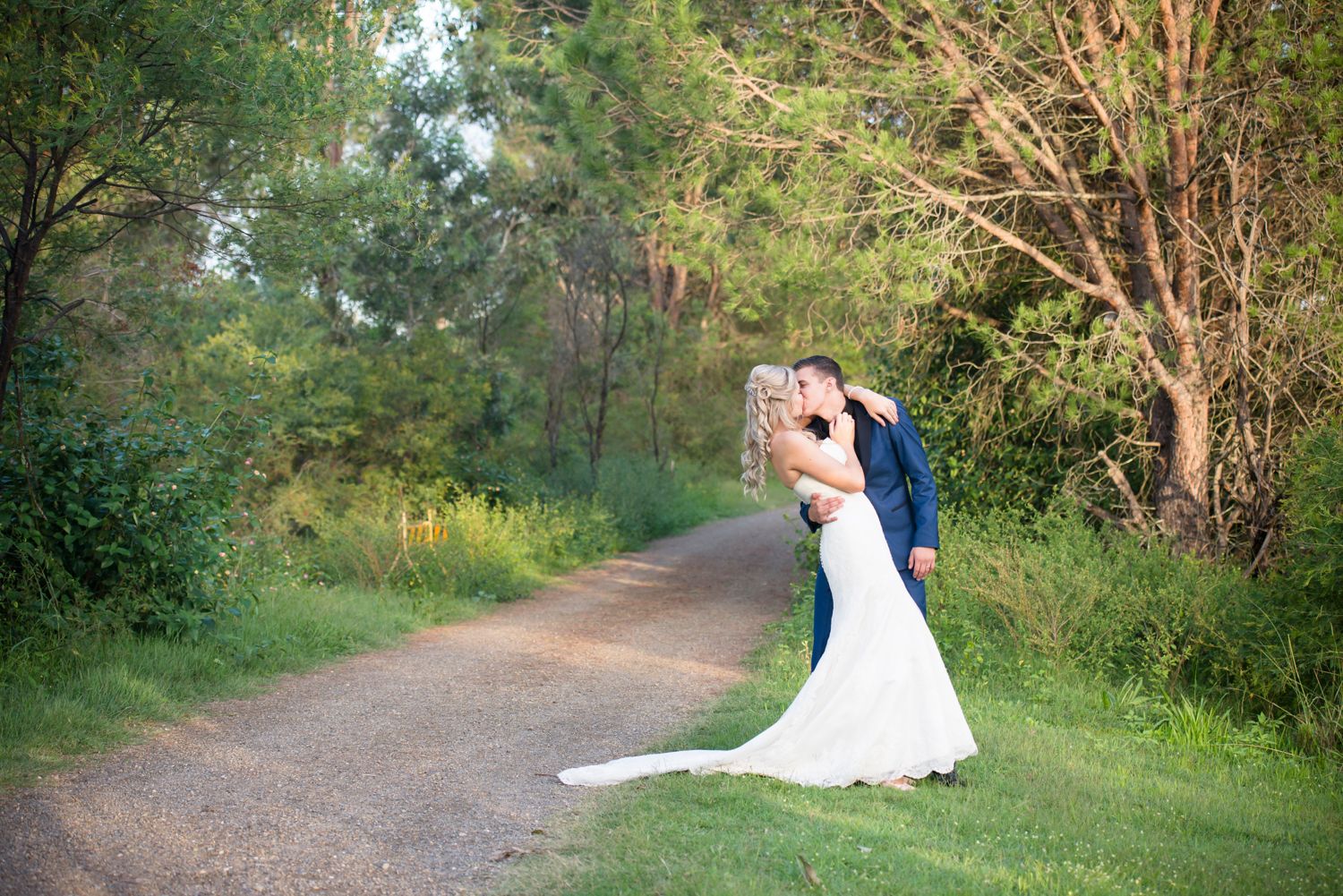Bride and groom shares a romantic moment on a tree-lined path in a natural outdoor setting.