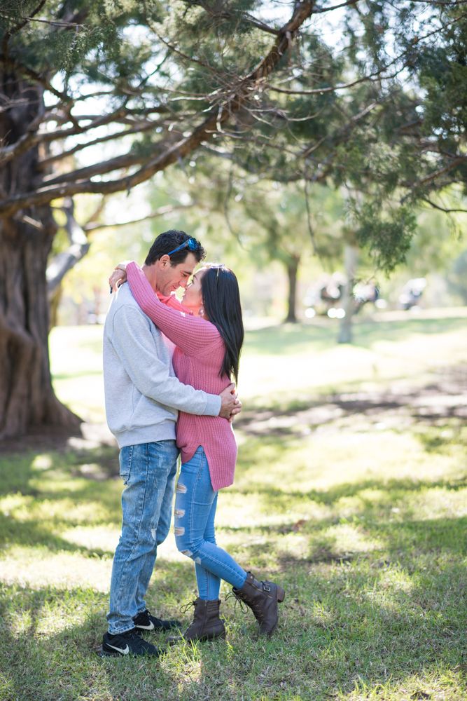 Playful couple shares sweet moments under pine trees in a park setting.