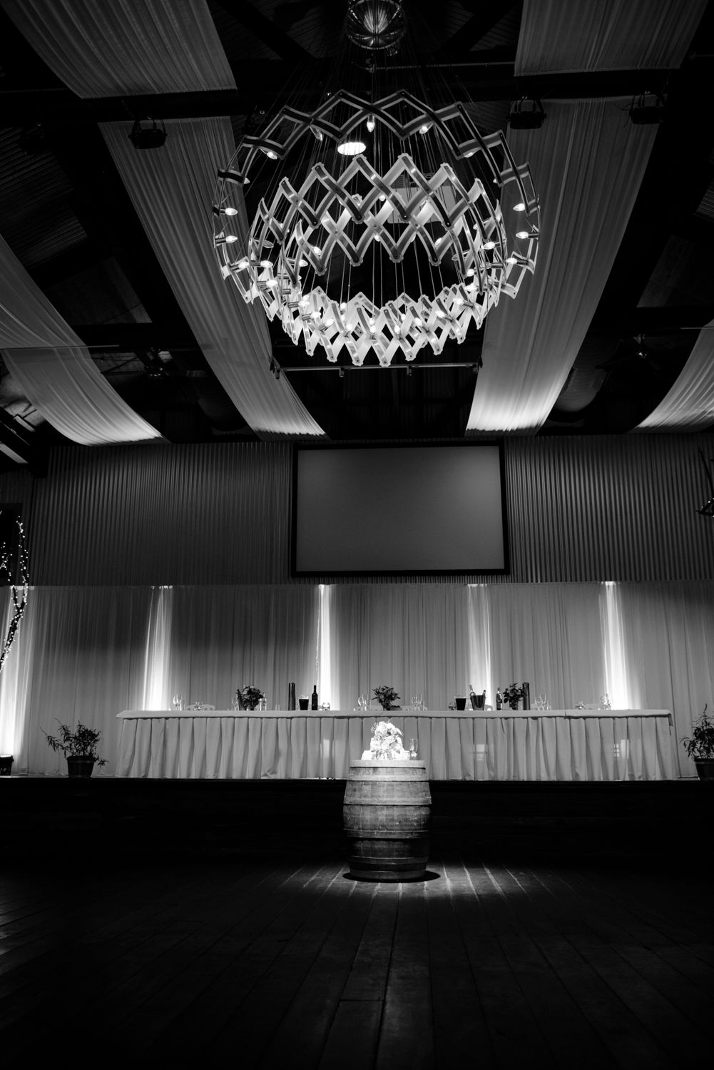 Black and white photos show a modern event space with geometric chandeliers and dramatic lighting on an empty stage.
