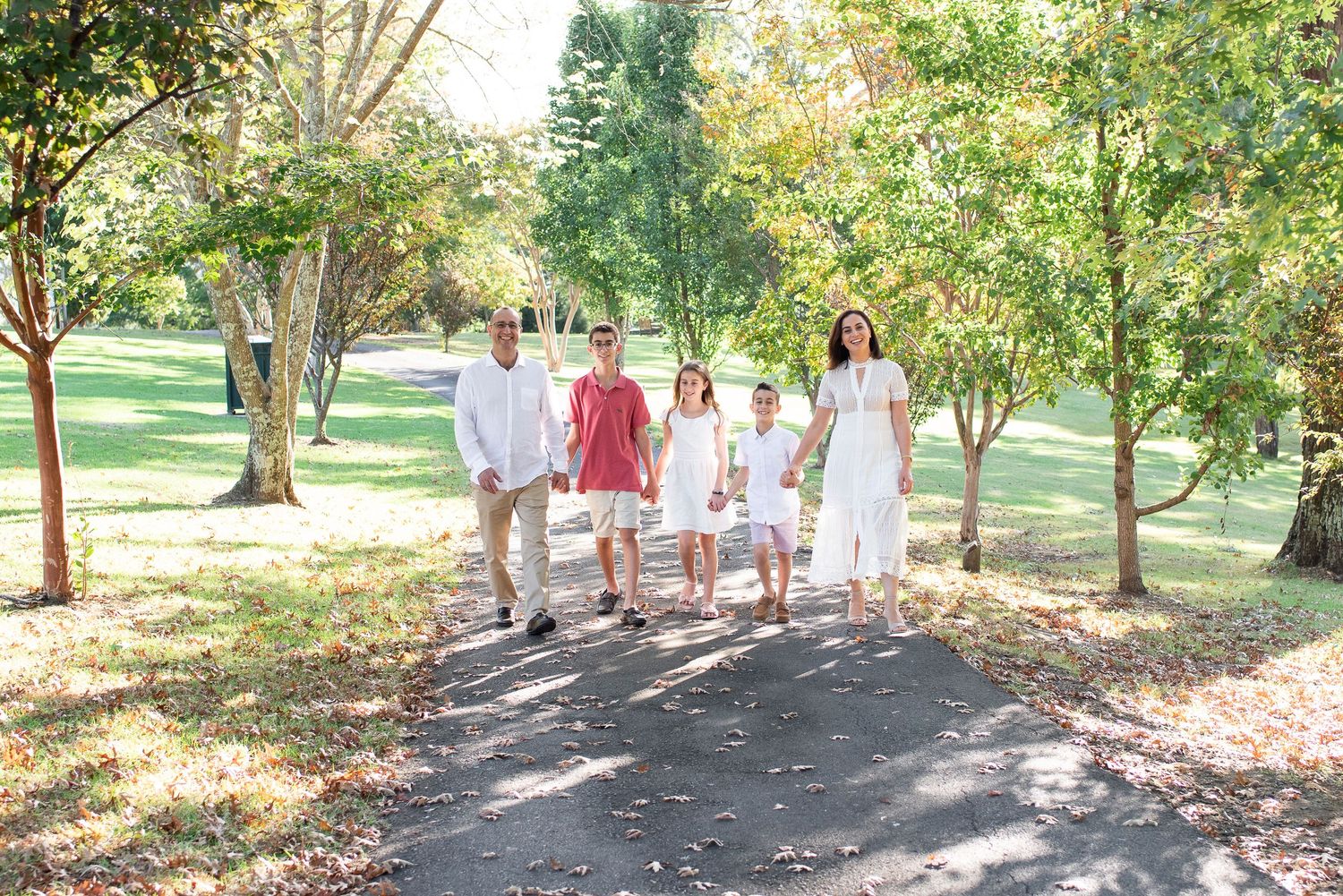 Family walks along tree-lined path during photo session.