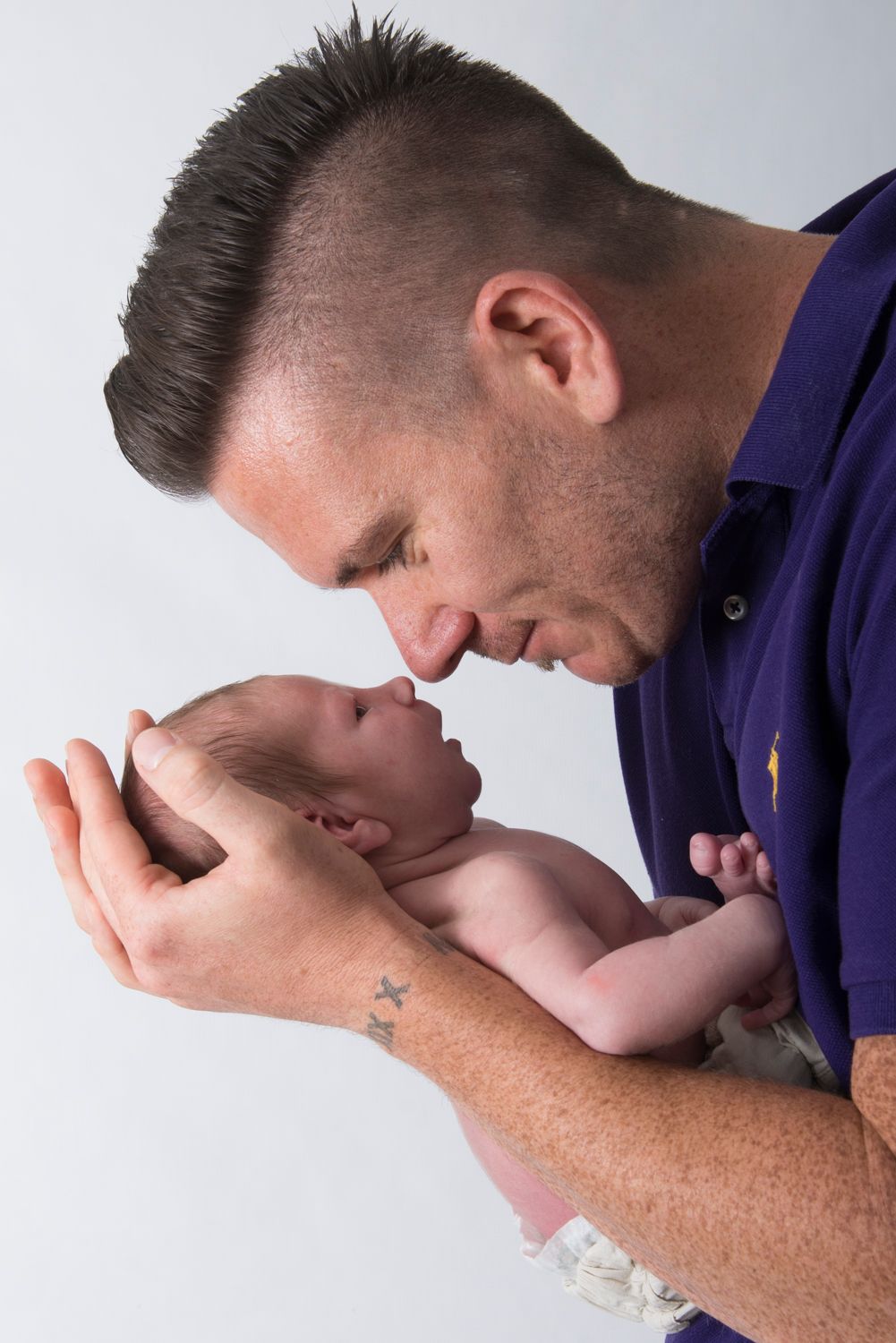 A tender moment between parent and newborn baby against a light background.