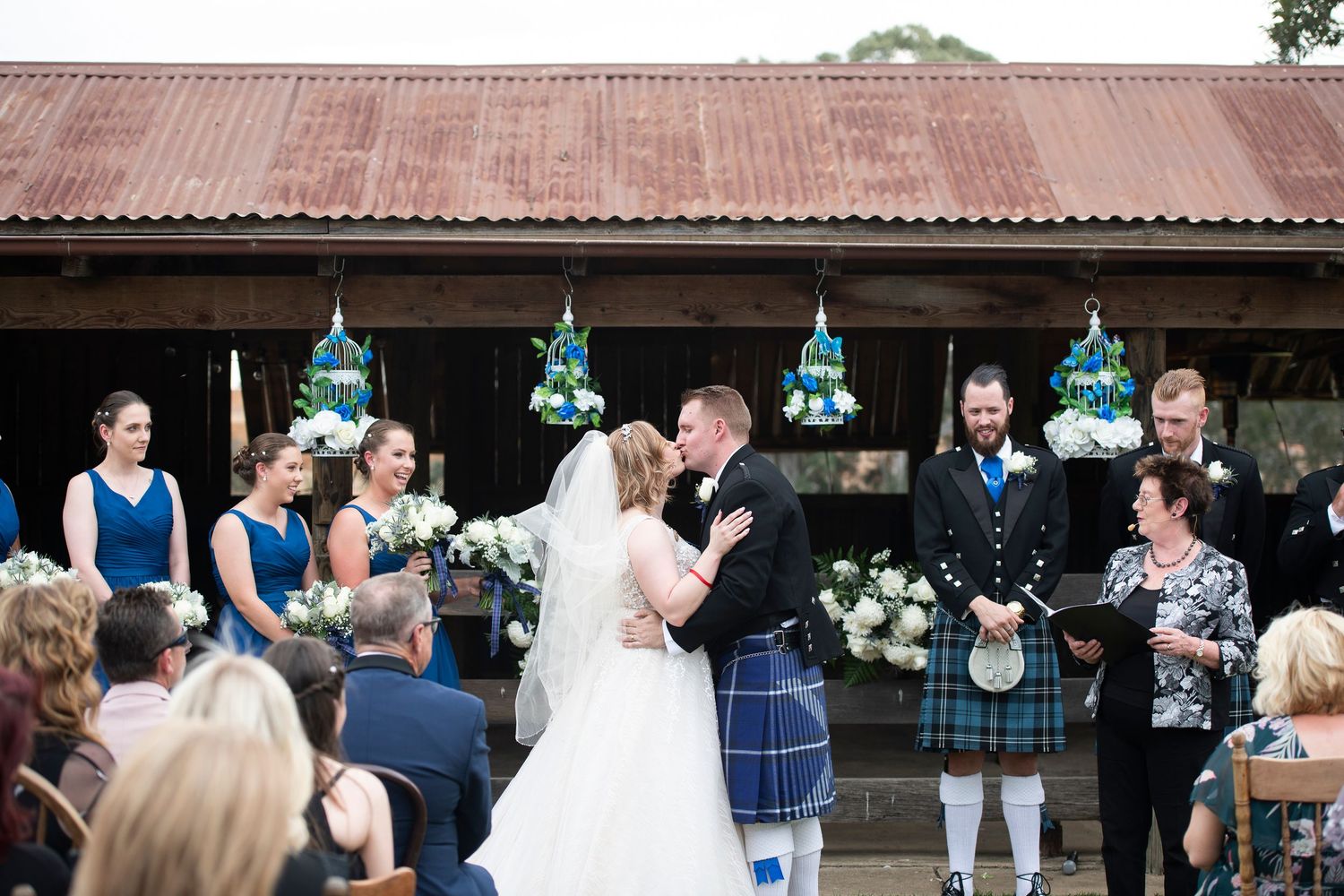 Wedding party celebrates with guests under rustic wooden pavilion roof.