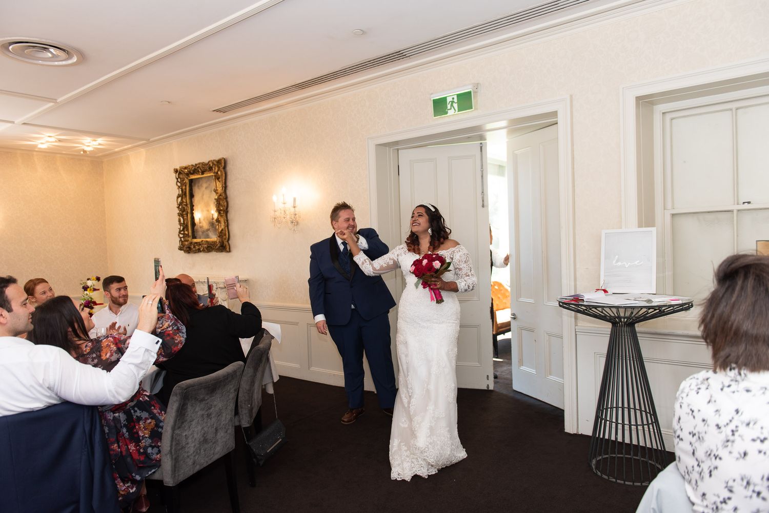Guests gather in an elegant white-walled reception at Dunbar House with ornate gold framed artwork and decorative lighting.