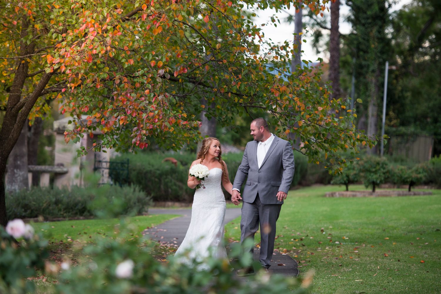 Wedding couple poses under vibrant orange autumn trees in park setting.