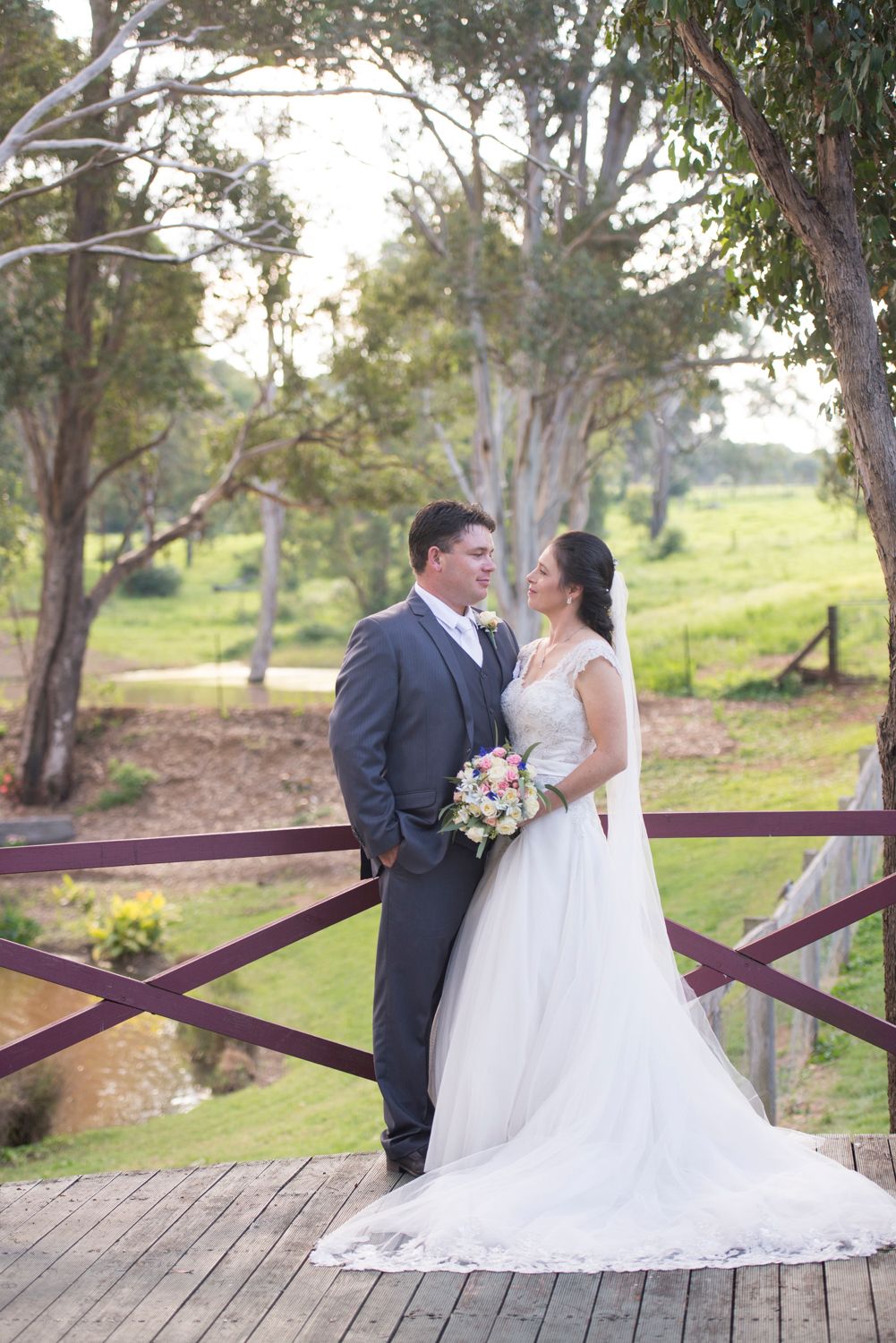 A romantic wedding couple shares intimate moments on a rustic wooden deck surrounded by eucalyptus trees.