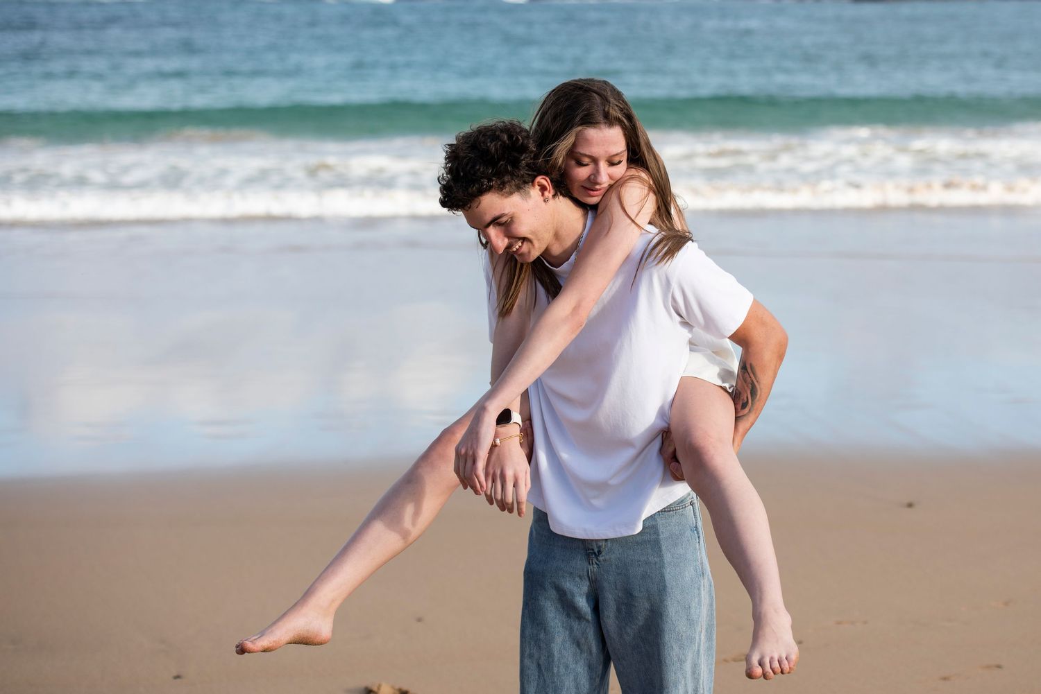 A Couple walking and playing together on a sandy beach in Kiama near blue ocean waves on a sunny day.