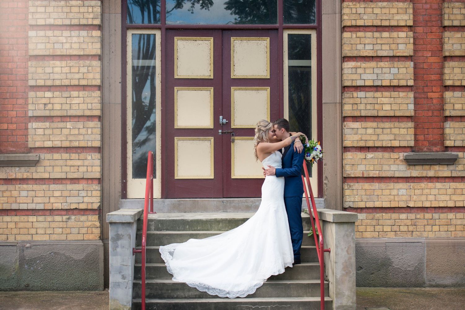 Wedding couple poses in front of historic brick building with architectural details.