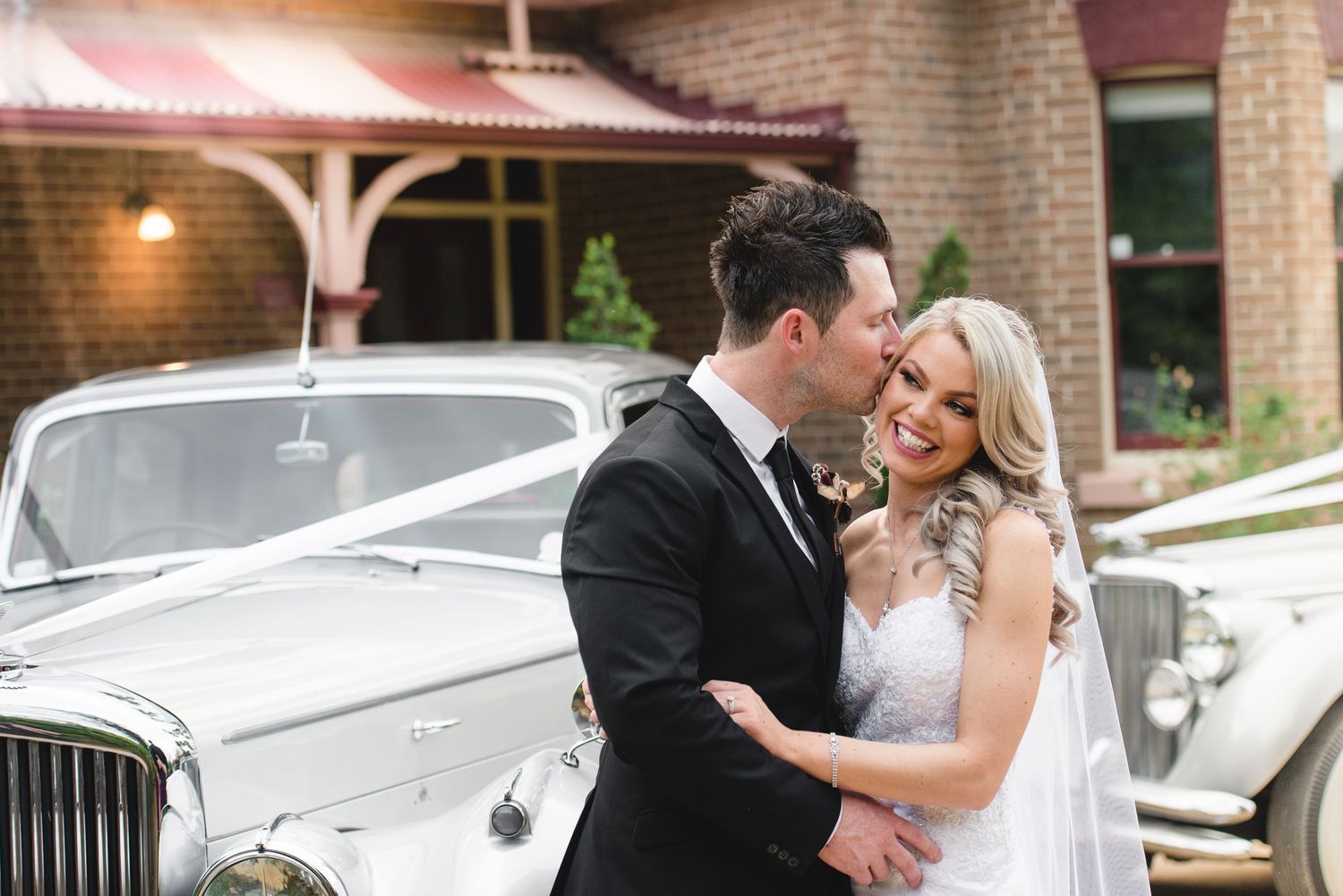 Elegant wedding couple poses together in front of a brick building during sunset.