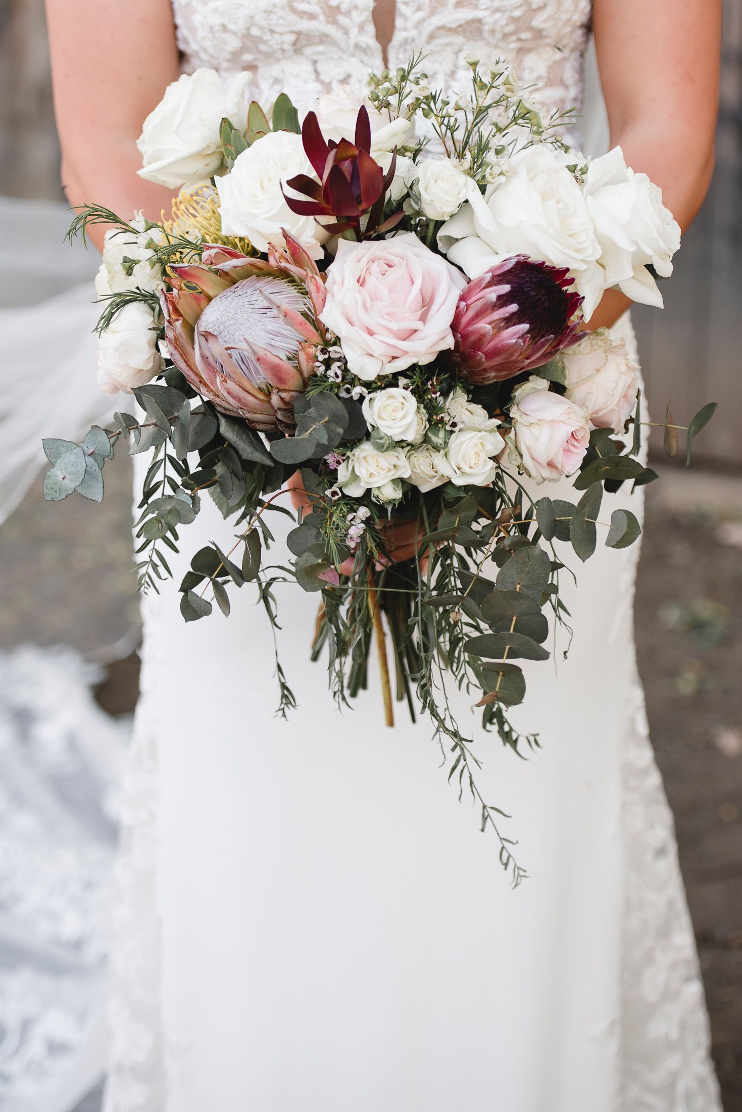Elegant bridal bouquet features white and burgundy flowers with cascading greenery.