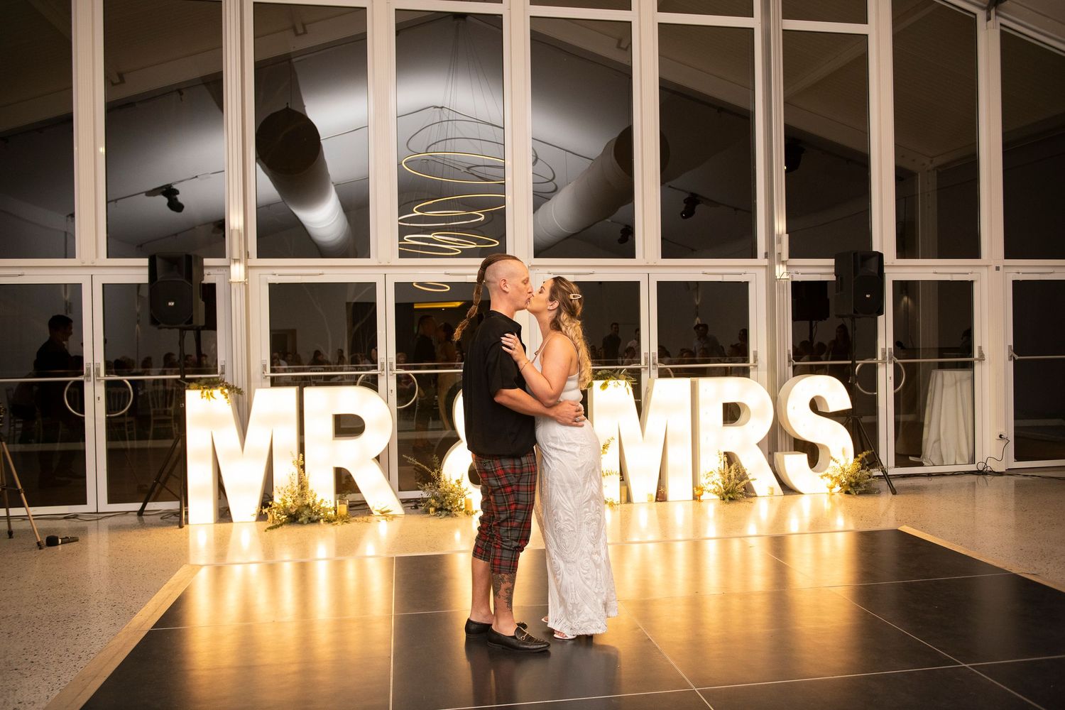 Illuminated wedding reception venue with glowing 'MR & MRS' sign and elegant table settings in a modern space.