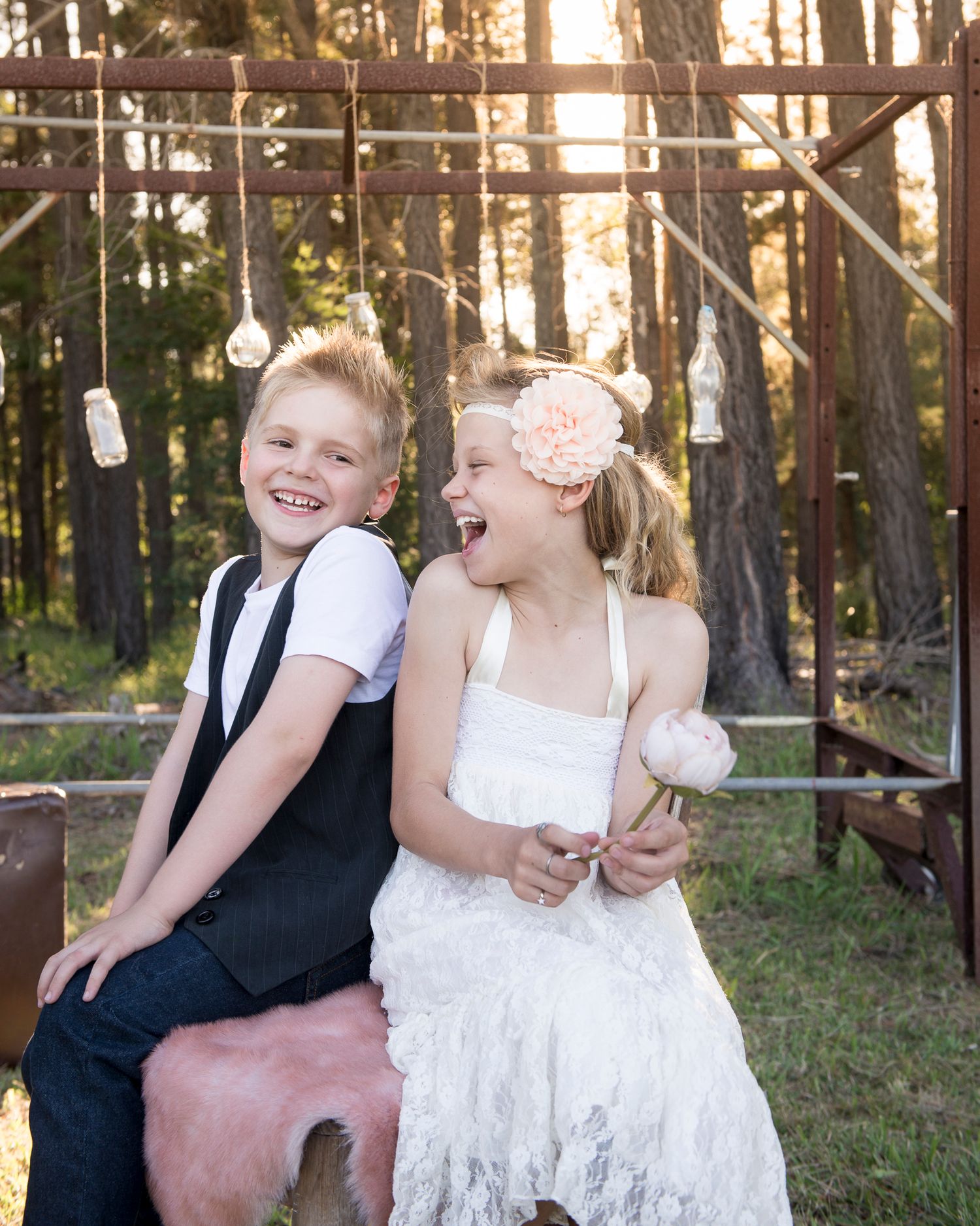 Children in formal attire play and laugh together in outdoor setting at sunset.