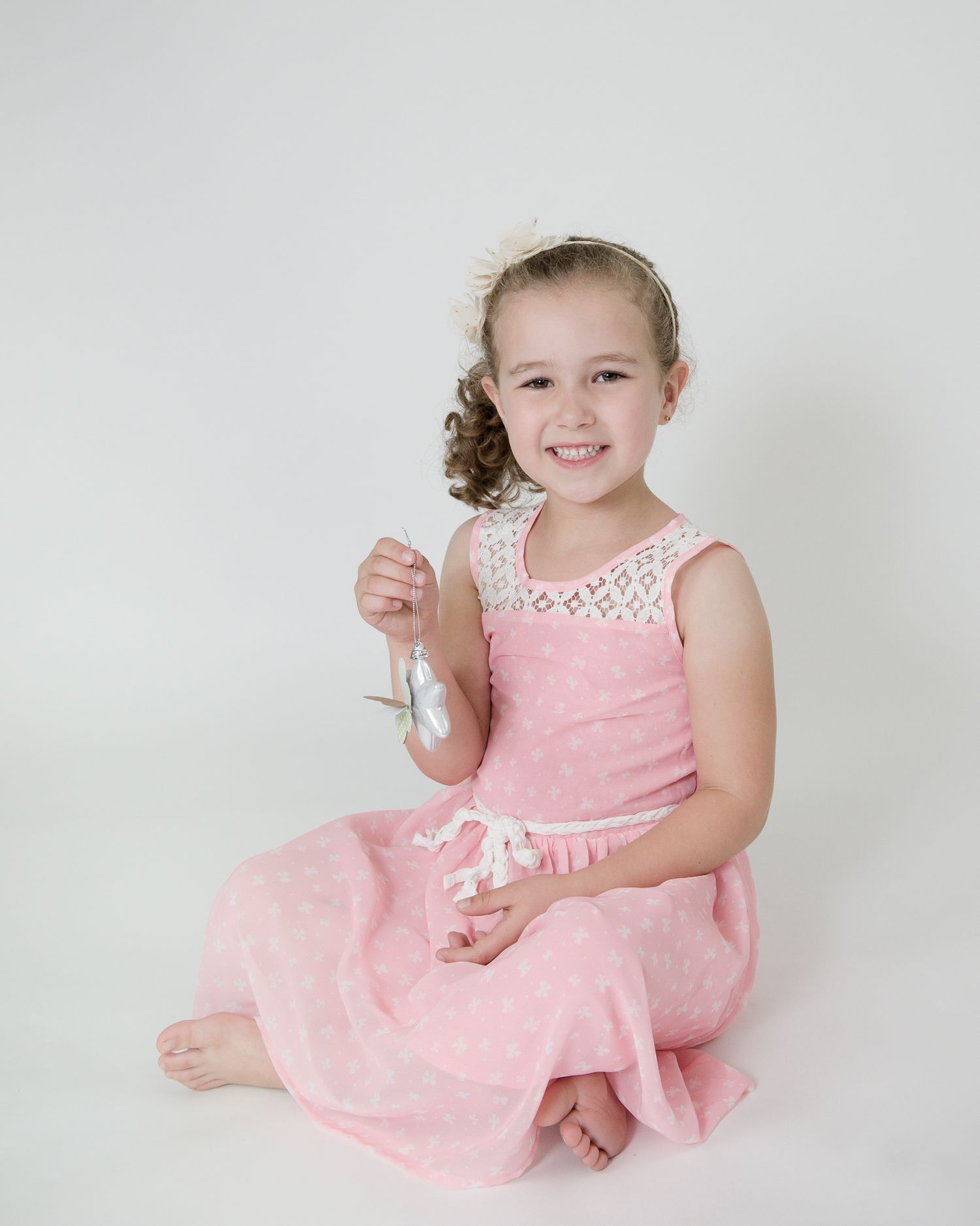 Young child in pink dress poses playfully in studio against white background.