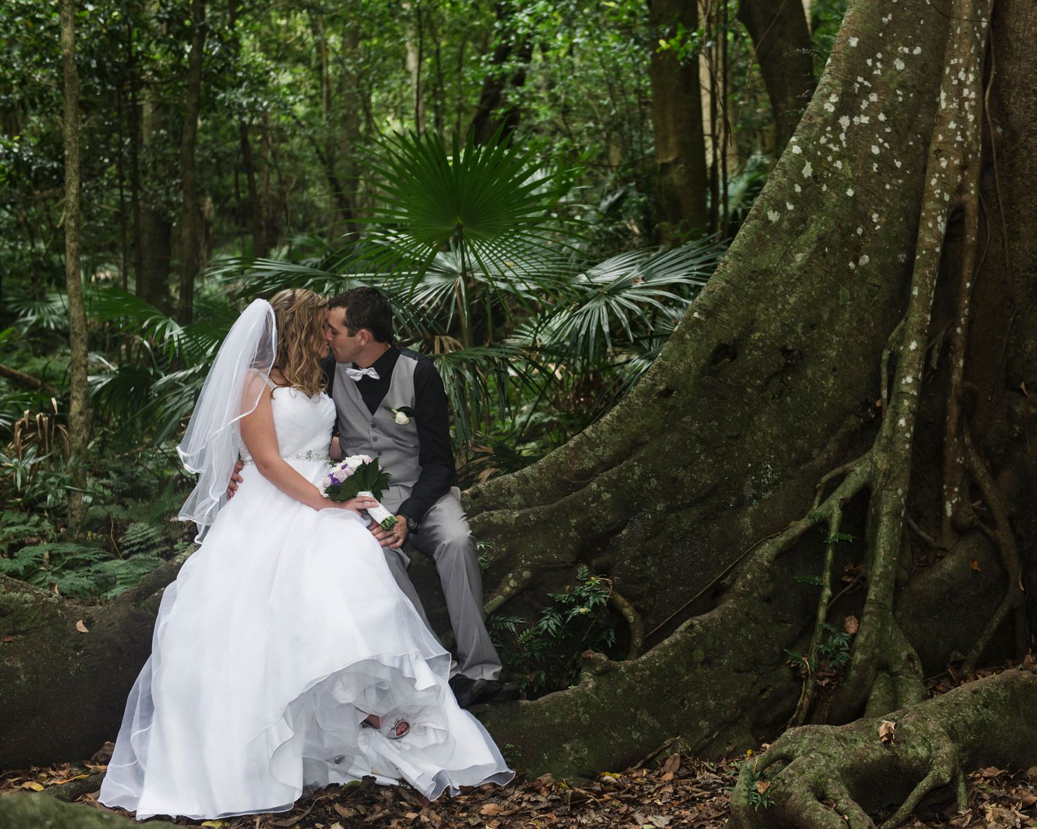 Couple poses for wedding photos in a magical forest setting with large tree roots.