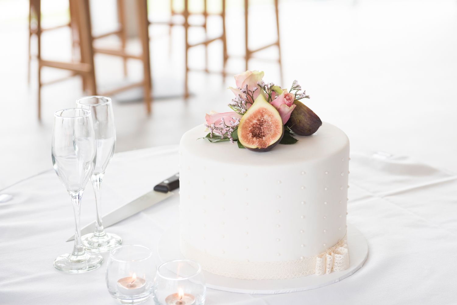 Elegant wedding table settings with white tablecloths, floral centre pieces, and a tiered white cake.