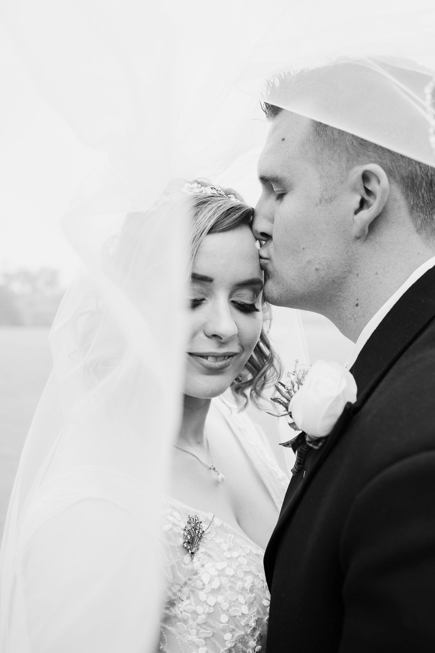 Intimate black and white portrait of newlyweds sharing tender moment under veil.