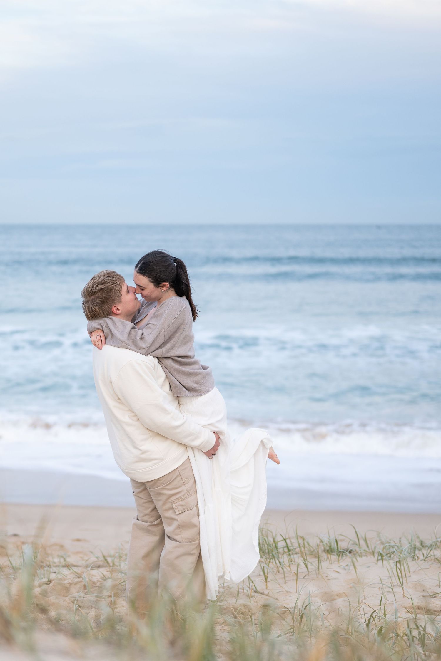 Romantic beach photoshoot with gentle waves and sea grass in the background.