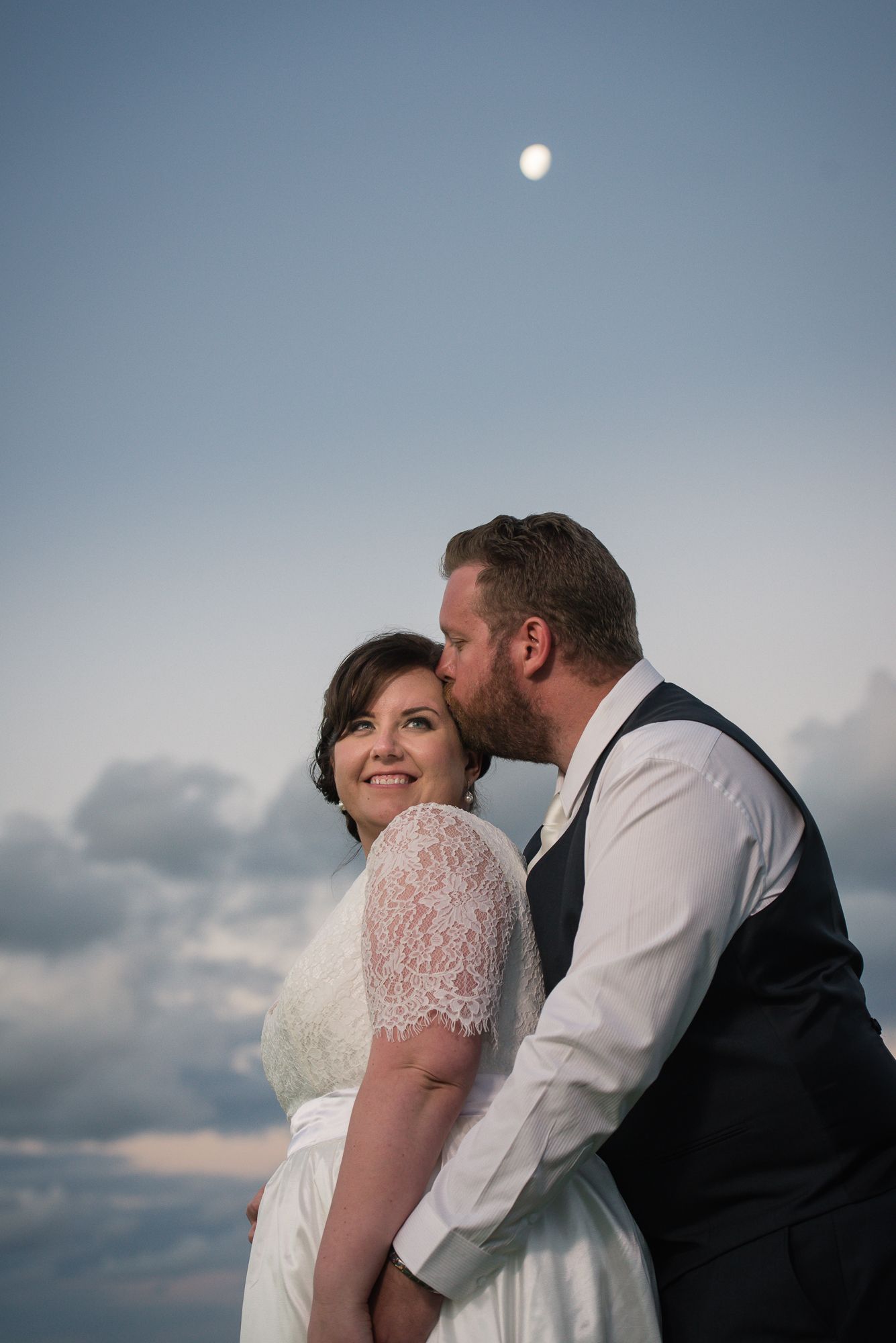 Intimate wedding couple moment captured against a serene blue sky at dusk.