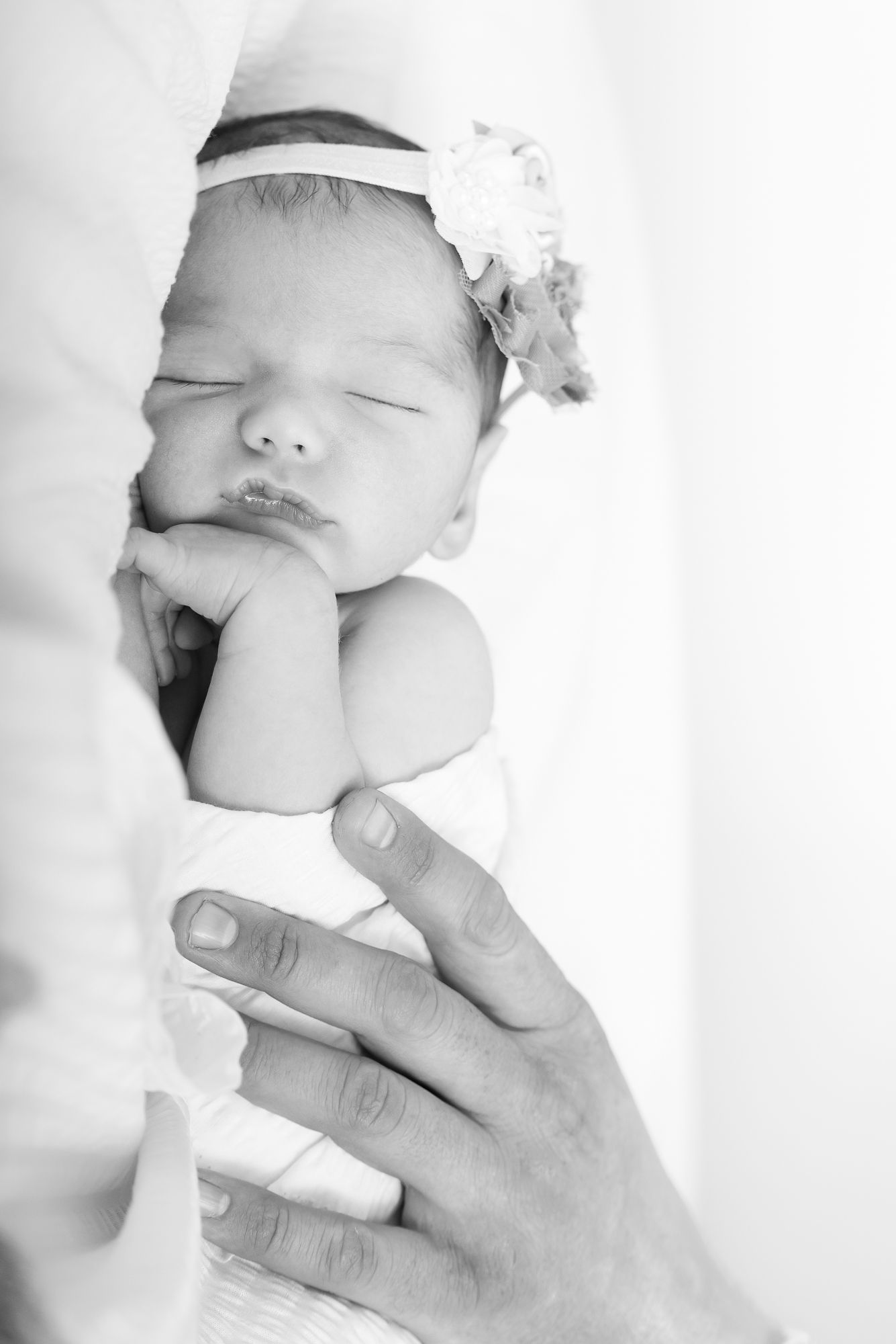 Peaceful sleeping newborn with white headband in black and white portrait.