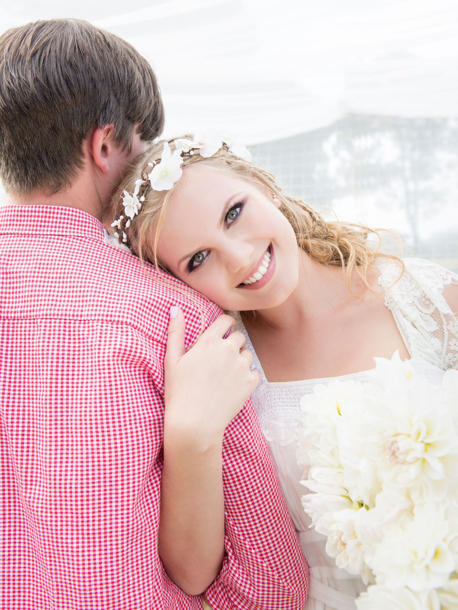 Romantic couple in red gingham and white dress sharing an intimate moment outdoors.