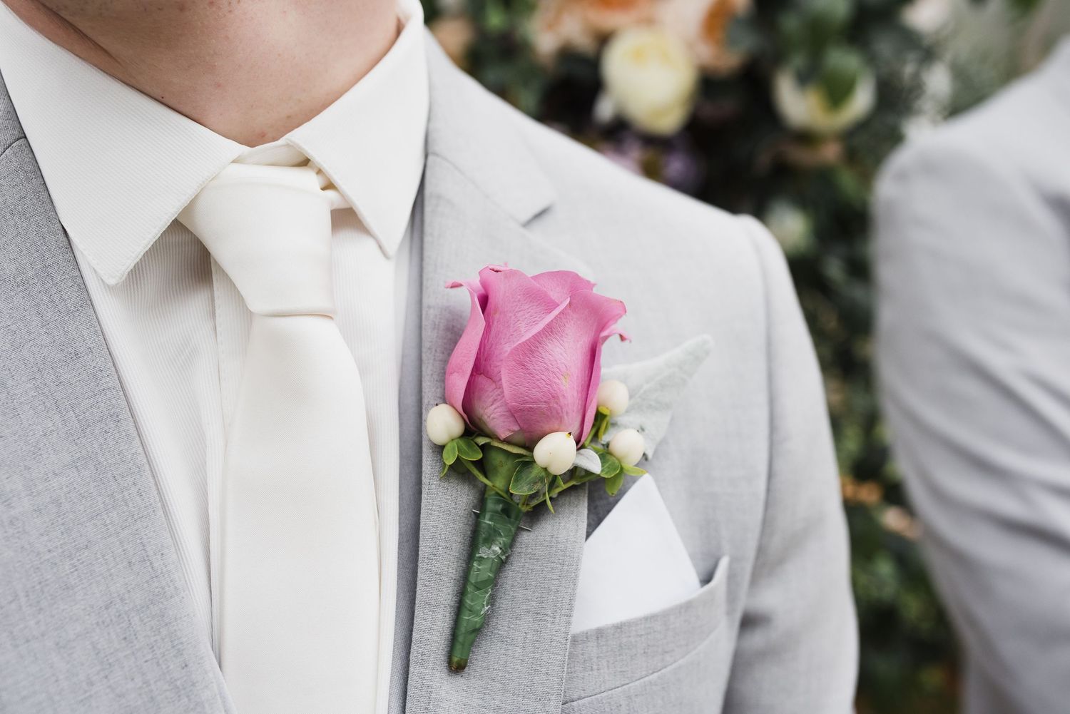 Groom in light grey suit with pink rose boutonniere stand in an elegant wedding ceremony.