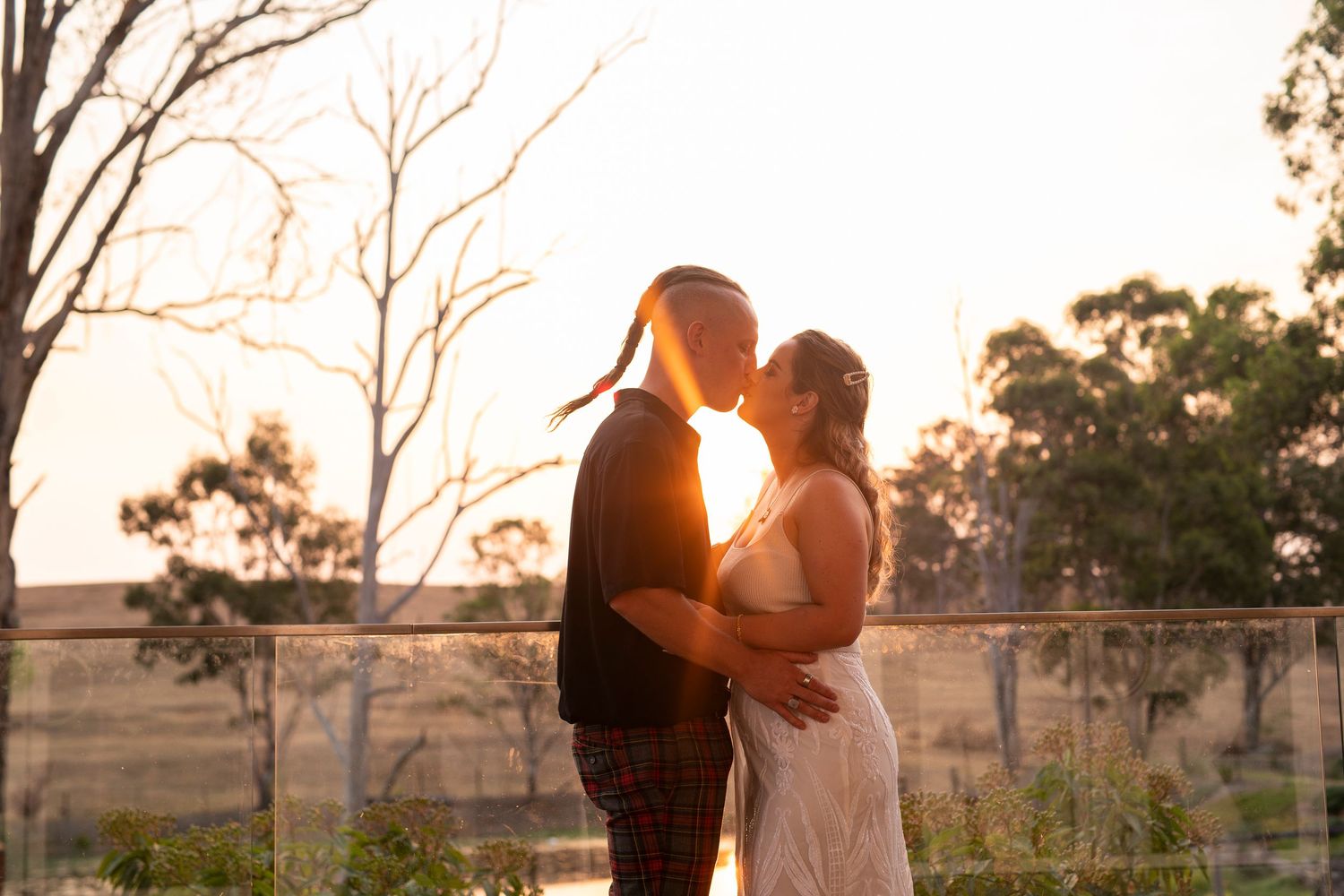 Silhouetted bride and groom embraces in a romantic sunset moment with golden light streaming through trees.