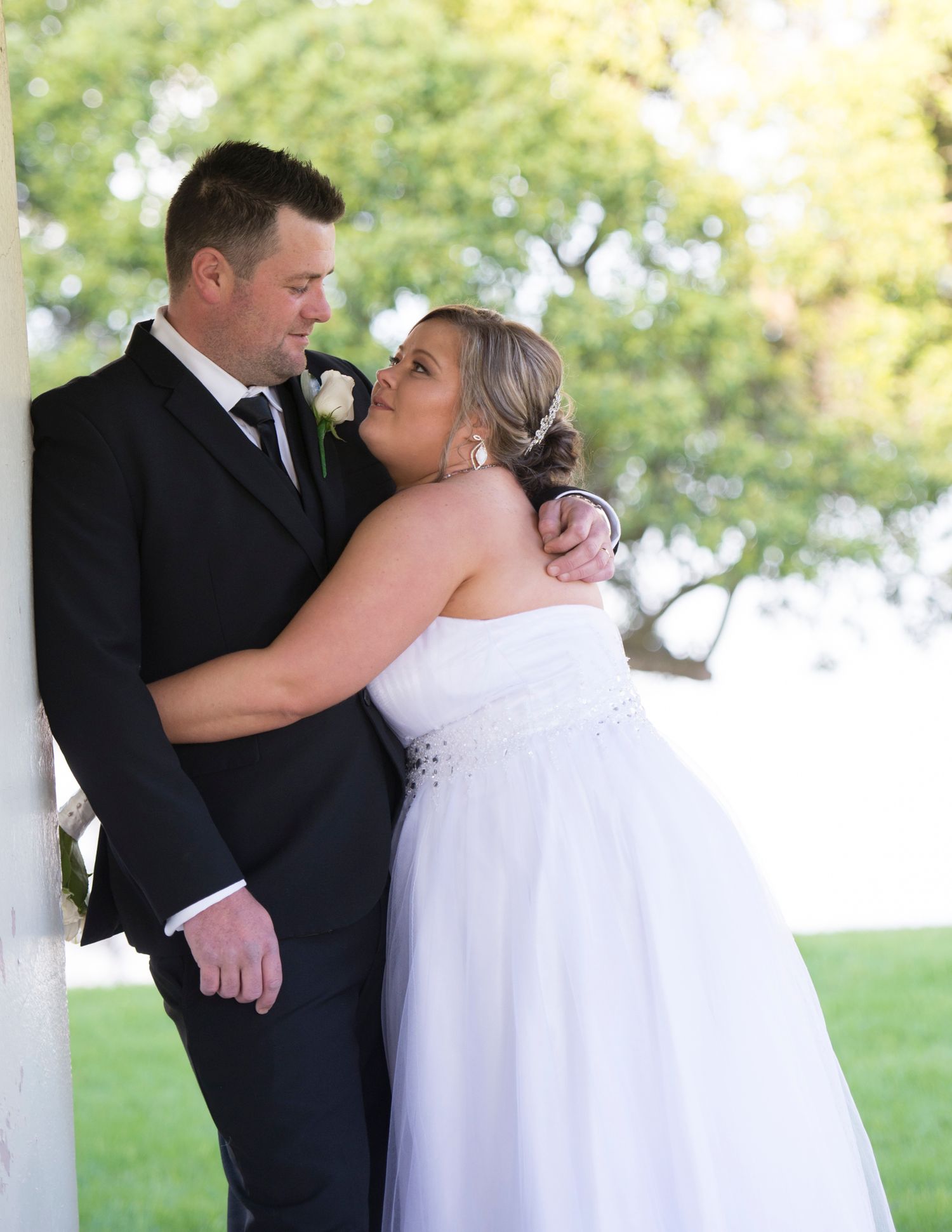 A romantic wedding couple shares a tender moment together in a white gazebo outdoors.