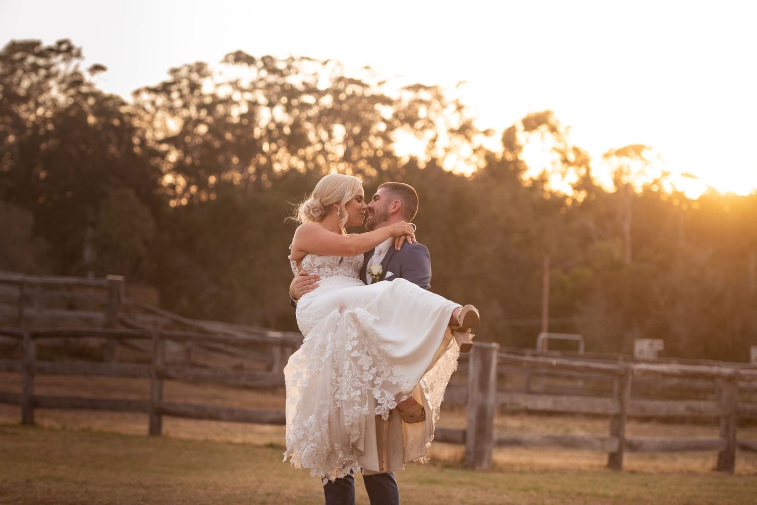 Romantic sunset wedding portrait against rustic wooden fence.