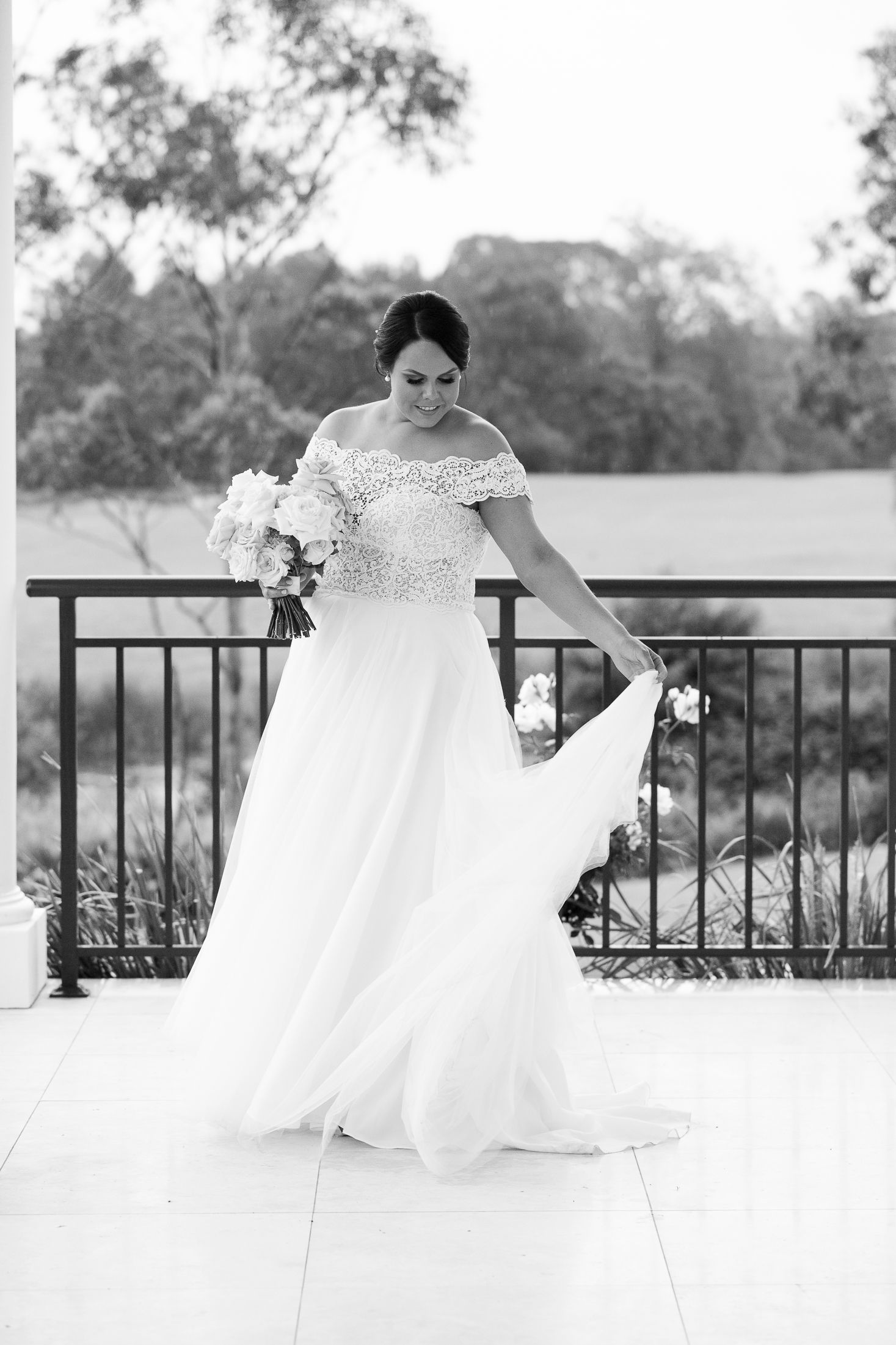 A bride in a flowing white wedding dress twirls gracefully on an outdoor balcony in black and white photography.
