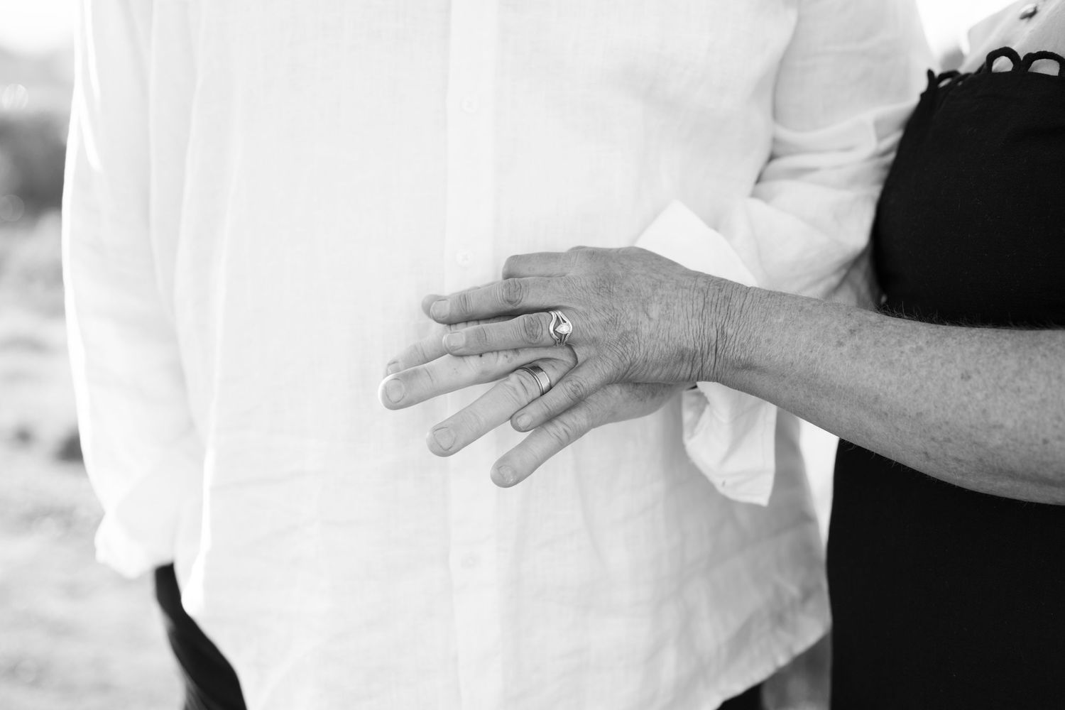 Black and white photo of couple holding hands showing wedding rings, romantic engagement or anniversary portrait.