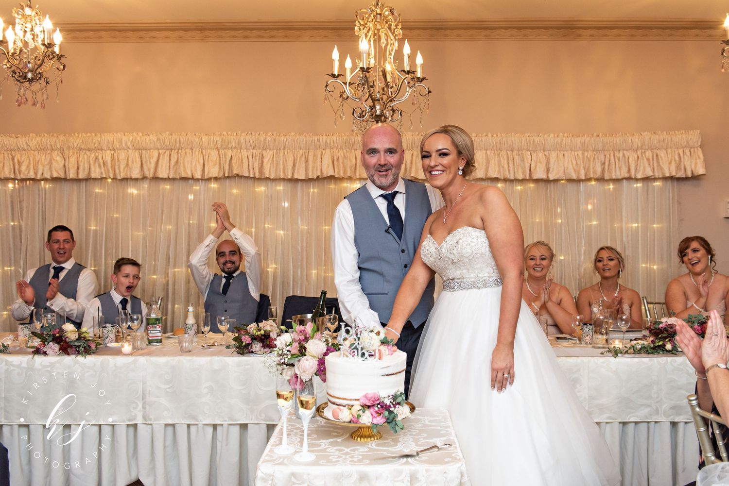 Wedding reception venue decorated with elegant chandeliers and white drapery for an indoor celebration.