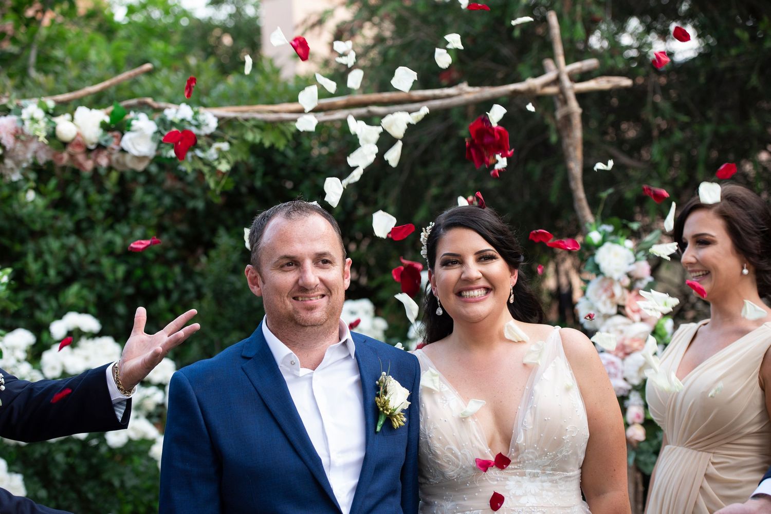 Wedding celebration with red and white decorative elements hanging from tree branches outdoors.