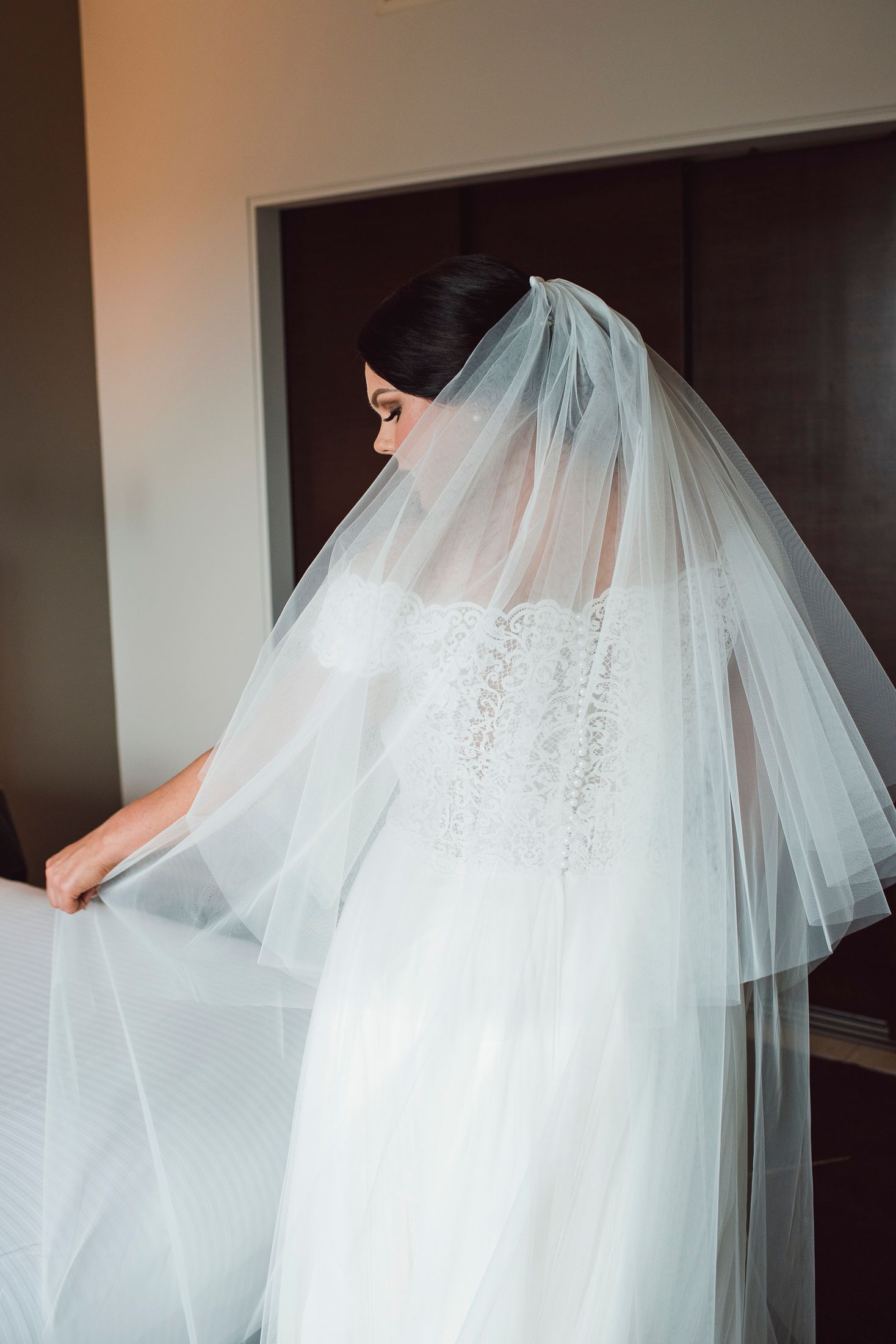 Flowing white wedding dress with delicate lace details and tulle veil captured in indoor lighting.