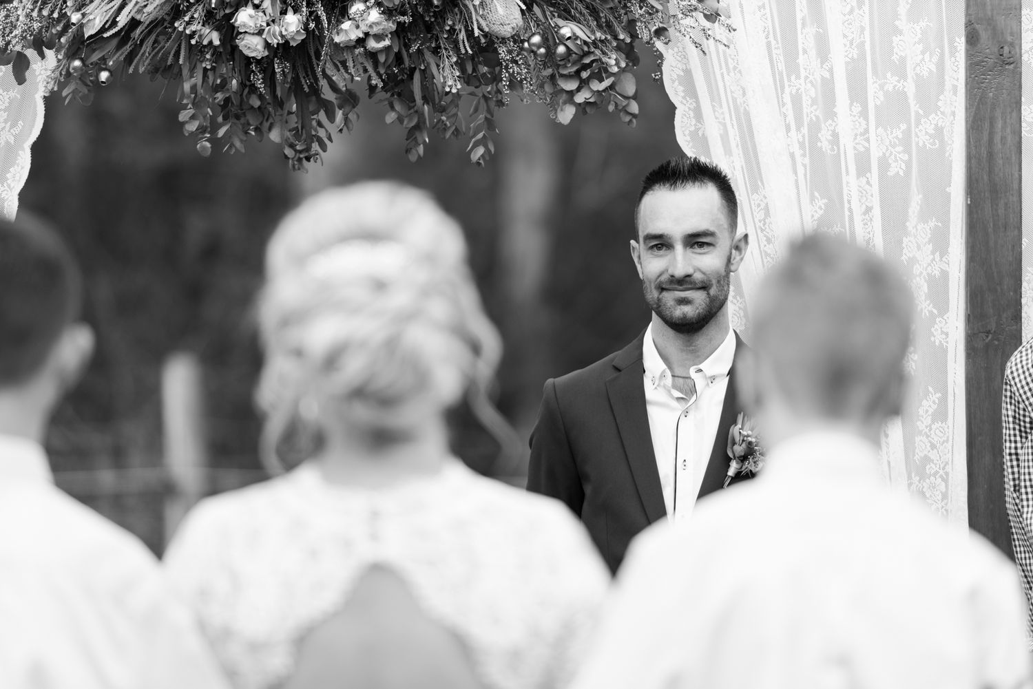 Black and white ceremony photo with elegant arch decorations and white draping.