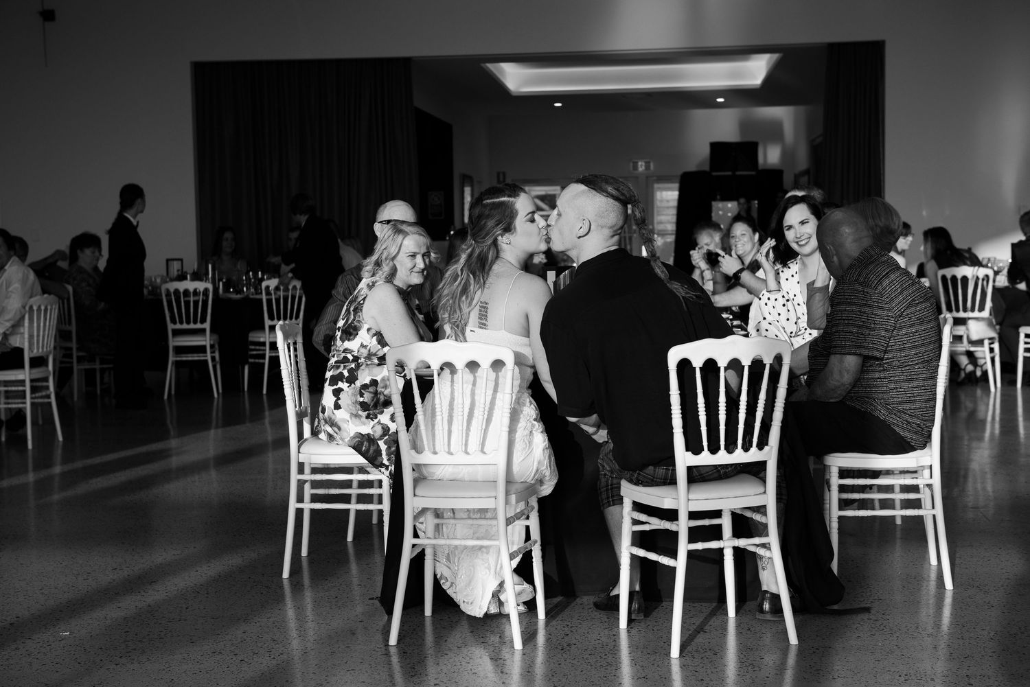 Black and white panoramic photo of a wedding reception venue with white chairs arranged around tables.