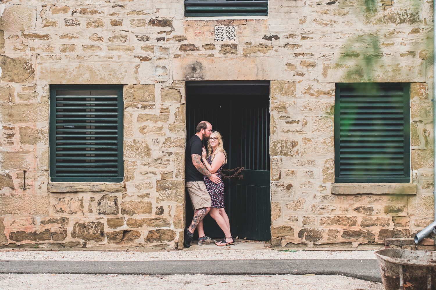 Two people share an intimate moment beside a stone wall with vintage green shutters.
