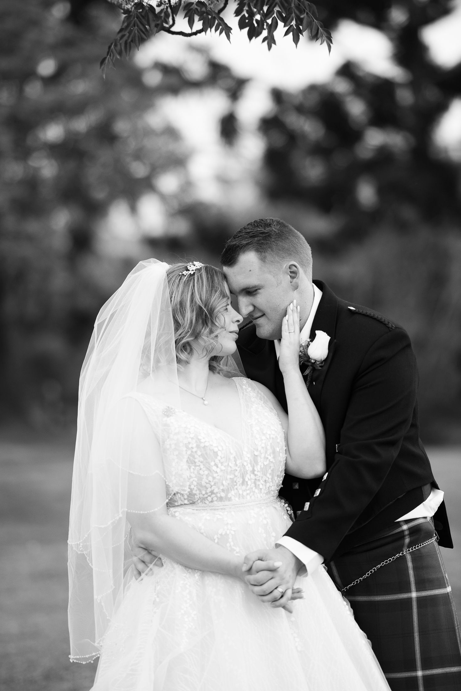 Black and white portrait of newlyweds sharing intimate moment in garden setting.