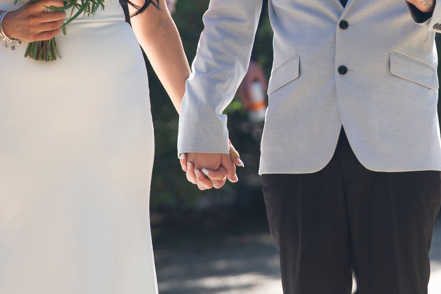 Close-up of wedding party members holding hands and bouquets against a natural backdrop.