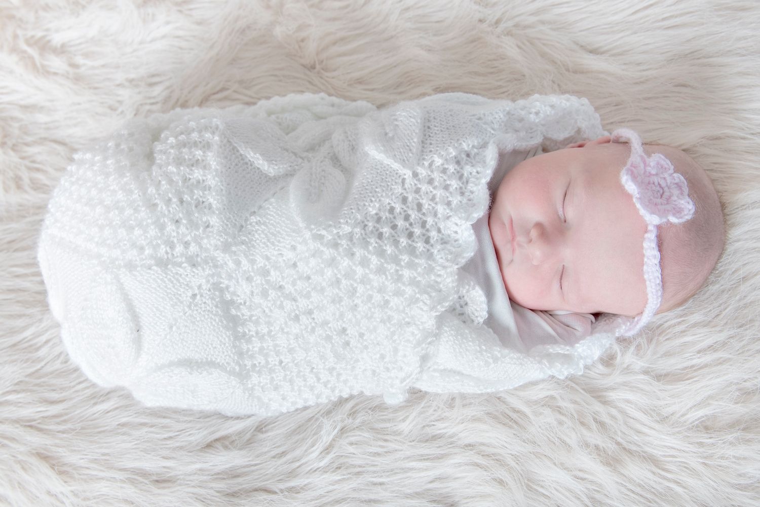 Newborn in white knit outfit sleeping on fluffy white rug.