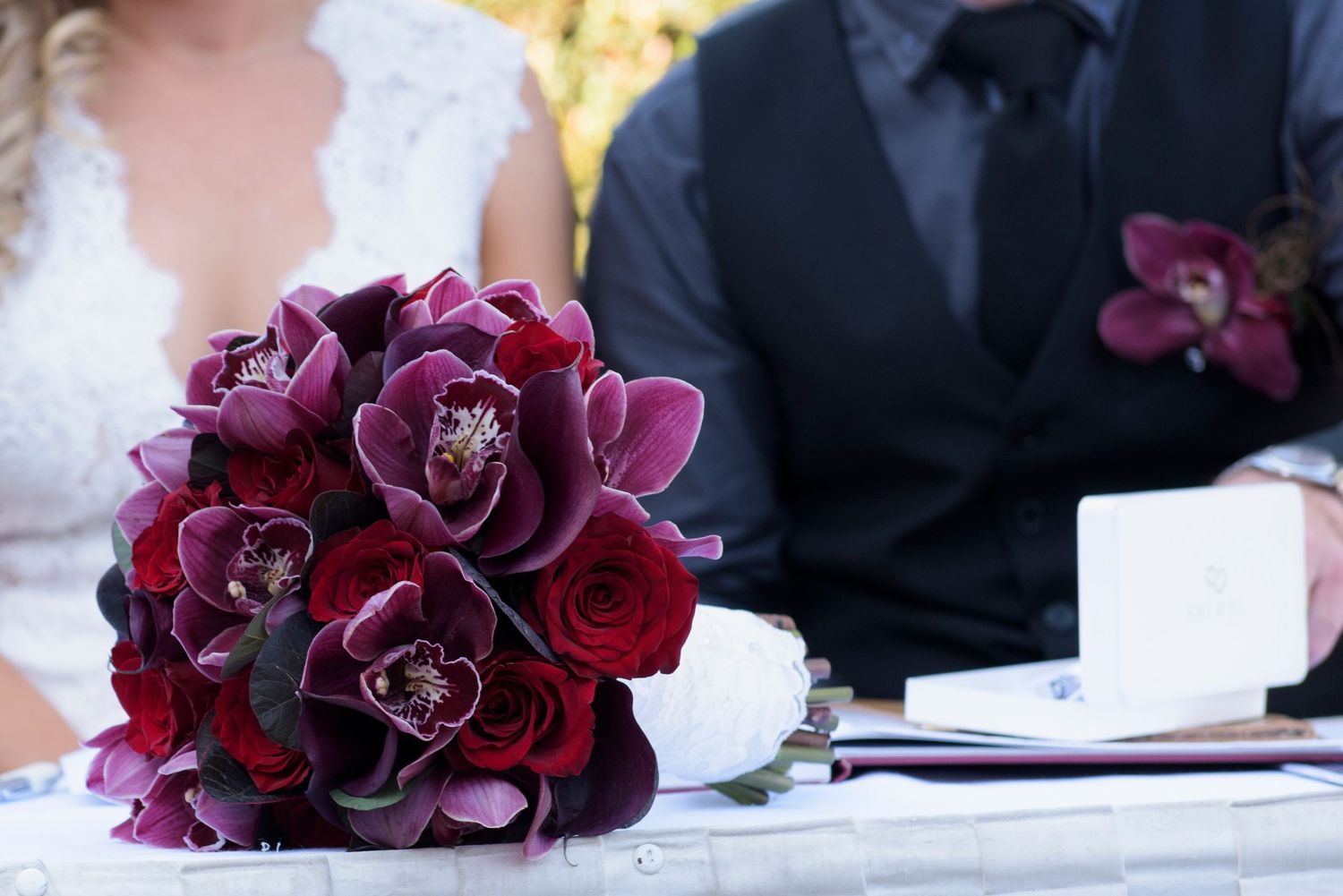 A deep burgundy and purple wedding bouquet with orchids and roses sits elegantly on a table.