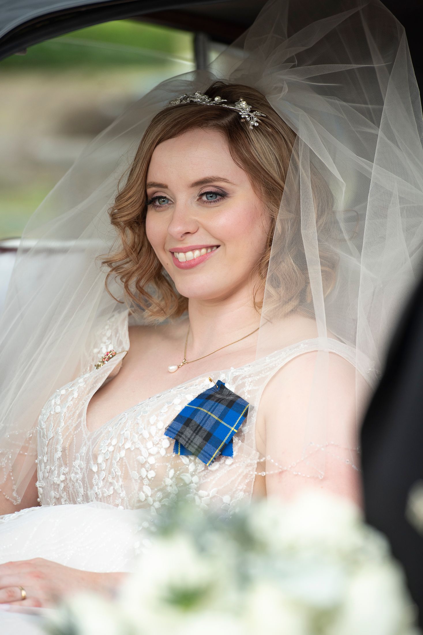 Bride wearing traditional white lace dress with flowing veil in car.