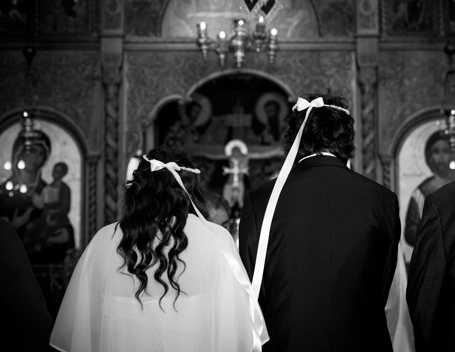 Black and white wedding photograph showing couple from behind during the Greek Orthodox wedding.