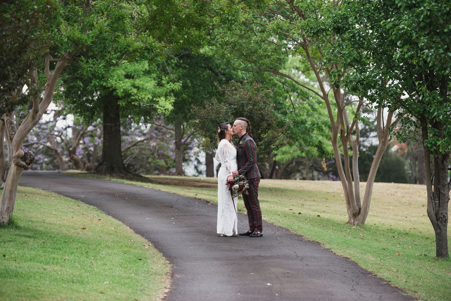 A couple stands together in a lush green park setting after their wedding ceremony.