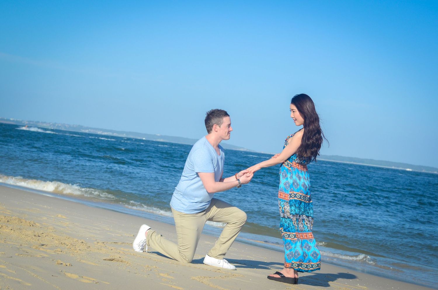 Beach proposal scene with ocean backdrop and bright blue sky.