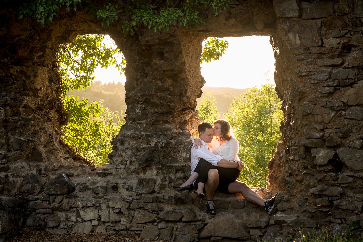 Silhouetted figures embrace in stone archway during golden sunset in Germany.