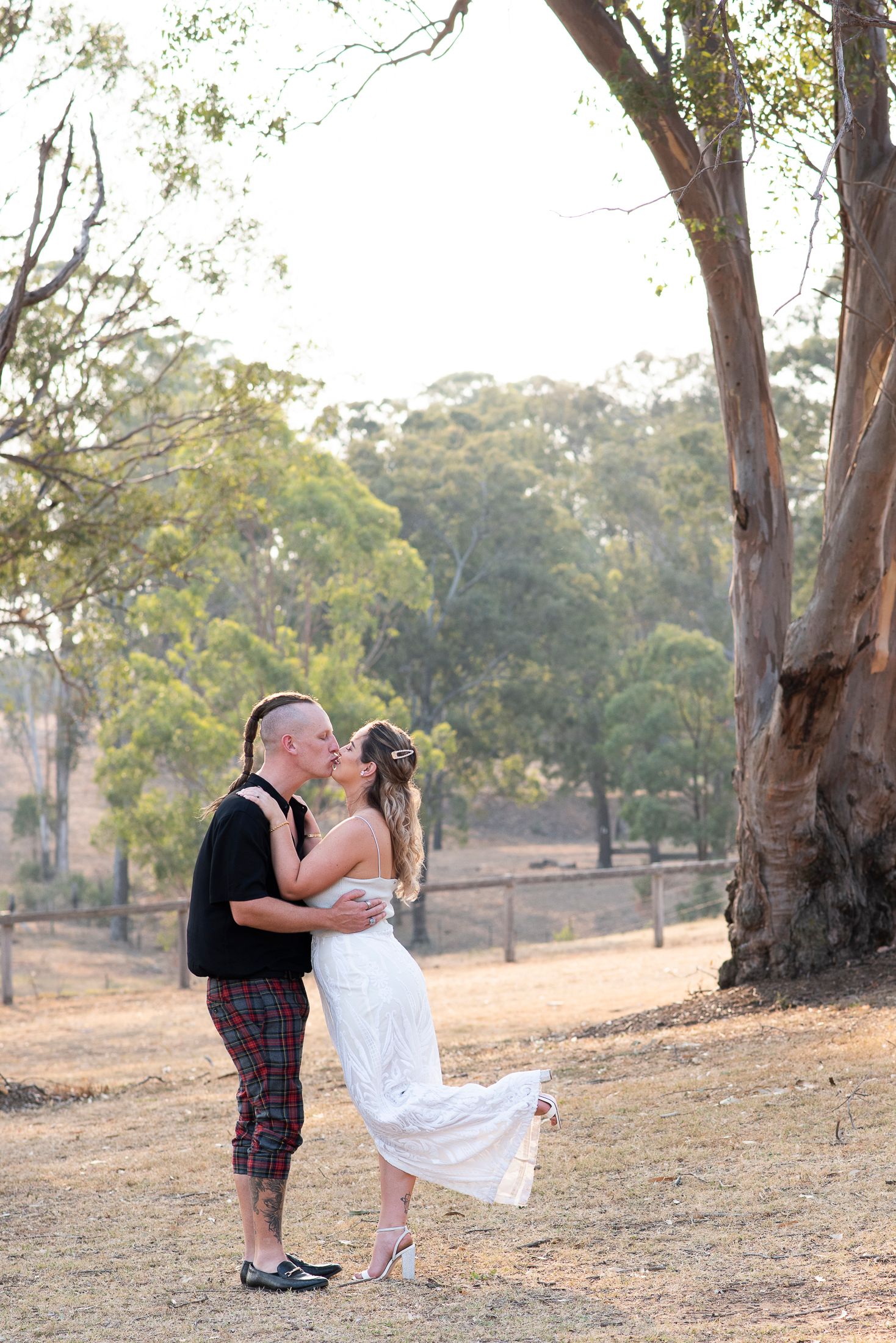 A couple shares a romantic moment during their ceremony in a rustic outdoor setting with eucalyptus trees in the background.