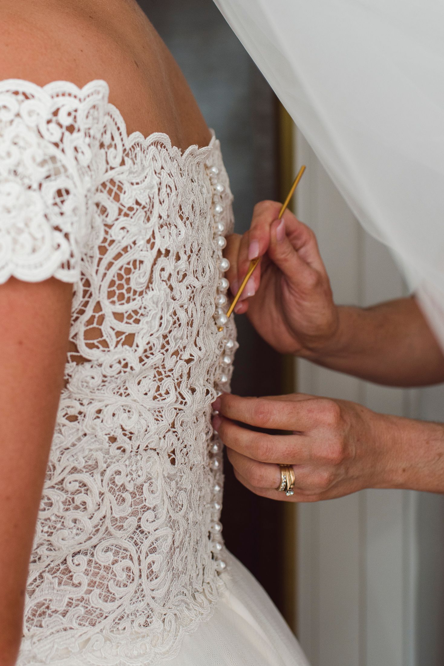 Close-up view of delicate white lace details being adjusted on a wedding dress bodice.