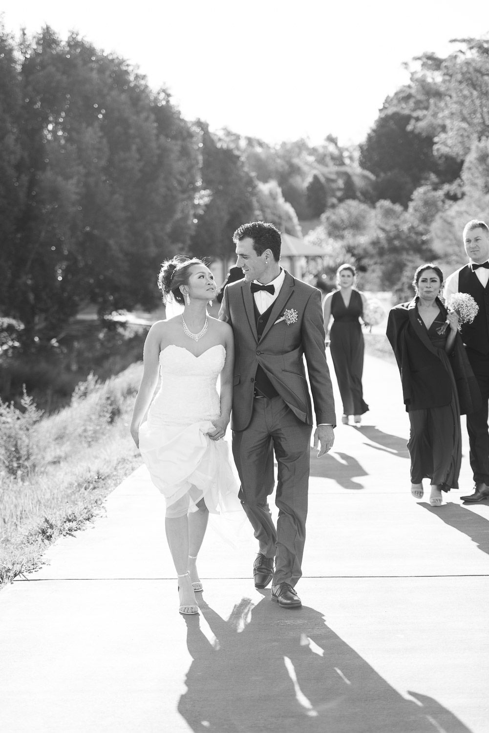 A black and white photo series shows a couple dancing and laughing together on a sunny outdoor path.